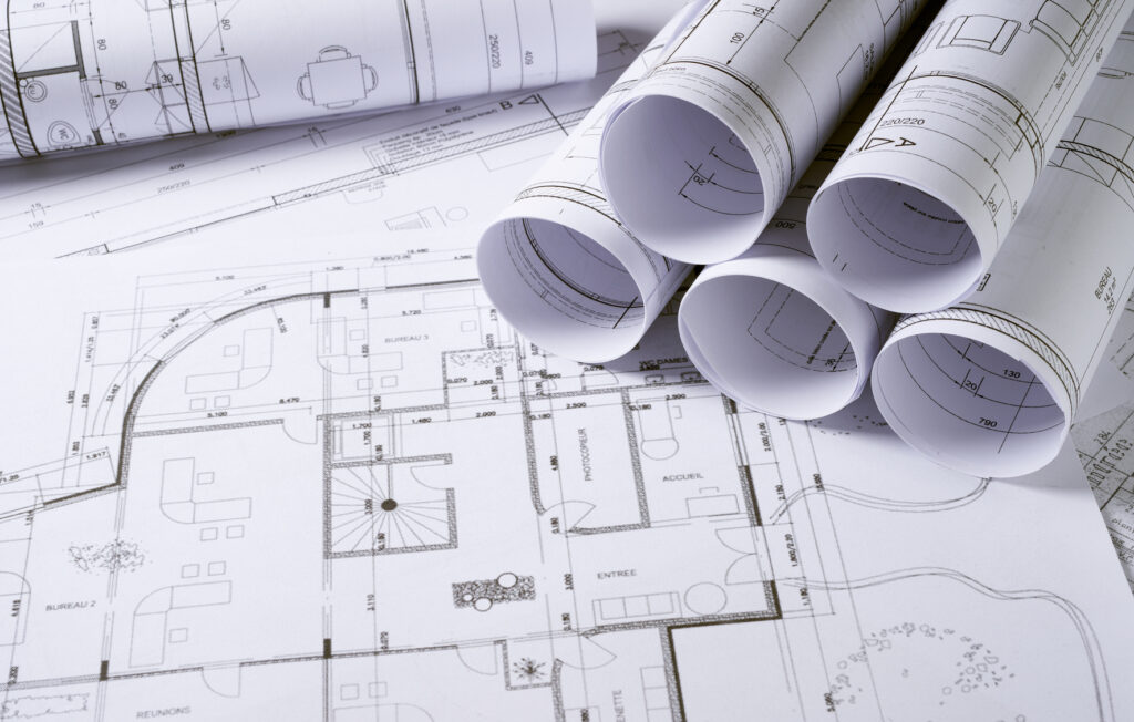 Plans architecturaux détaillés avec plusieurs rouleaux de plans posés sur une table.